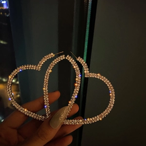 Close-up of large gold heart-shaped earrings with rhinestones against city lights