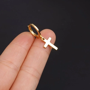 Close-up of a gold cross pendant earring held against a solid black background