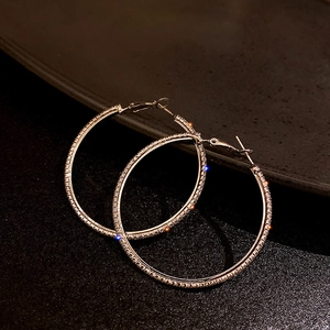 Dettaglio di grandi orecchini a cerchio in argento con strass lucidi su sfondo nero