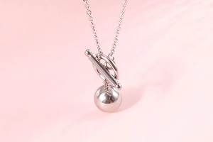 Macro view of silver bead necklace with T-bar toggle clasp on a pink background