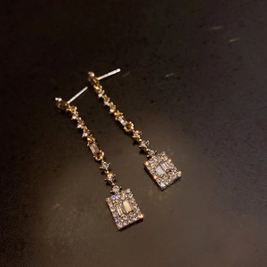 Detailed macro view of gold-plated earrings with rectangular zircon crystals and small rhinestones