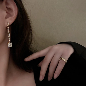 Macro shot of gold geometric drop earrings with crystals and a Cuban link style ring