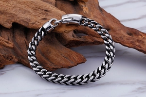 Detailed close-up of a silver woven titanium steel chain bracelet on a wooden display