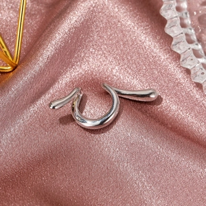 Macro shot of silver-tone snake-style ear cuff with sleek waterdrop detail on pink satin