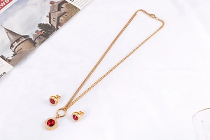 Detail eines goldenen Schmucksets mit roten Kristallanhängern und Ohrsteckern auf Stoff