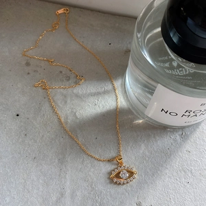 Macro shot of gold-plated evil eye necklace with pave crystals on minimalist grey background