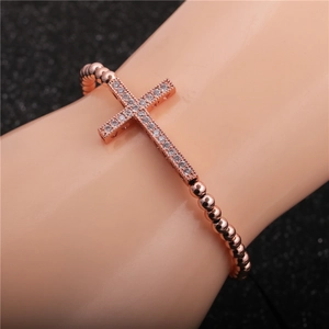 Macro detail of rose gold cross bracelet with micro-paved zircons and metallic beads