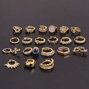 Set of nine pairs of gold geometric huggie earrings with zircons on dark background