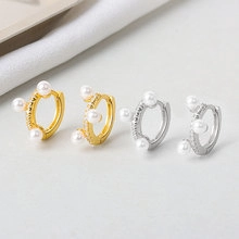 Detail view of gold and silver hoop earrings featuring three small white pearls set in metal