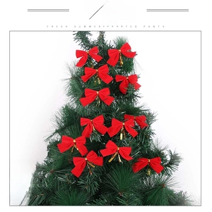 Close-up of red Christmas bow ornaments hanging on a green festive tree branch