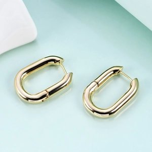 Macro detail of polished 18K gold-plated U-shaped oval hoop earrings on light blue background