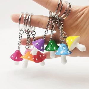 Colorful resin mushroom keychains with white dots and silver metal rings held in hand