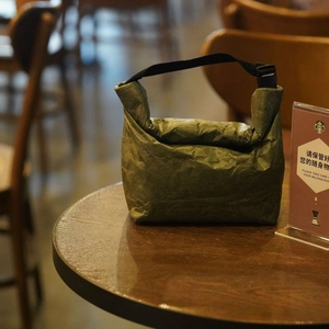 Waterproof Tyvek lunch bag in dark green with adjustable black shoulder strap on wooden table