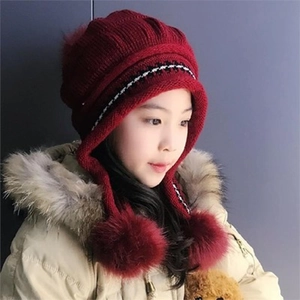 Close-up of red winter knit hat with large pom-poms and warm ear flaps for kids