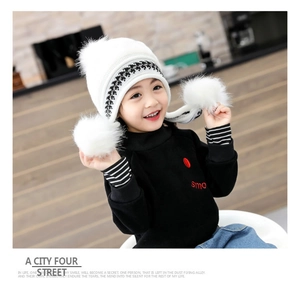 Close-up of white knitted hat with fuzzy pom-poms and black turtleneck sweater on child