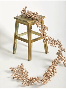 Détail d'une guirlande de baies dorées de 2m drapée sur un tabouret en bois vert rustique