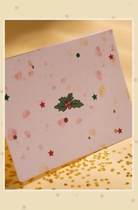 Close-up of pink Christmas card with holly and gold star sequins on silk fabric