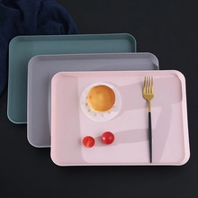 Three minimalist rectangular plastic trays in pink, grey, and dark green with anti-slip edges