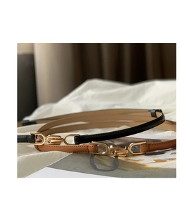 Detail of two slim black and brown leather belts with polished gold interlocking buckles
