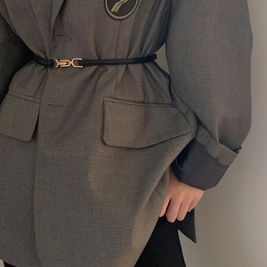Detail of slim black leather belt with gold metal buckle on a grey blazer jacket