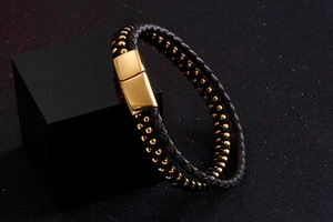 Detail of double-layer black braided leather bracelet with gold beads and metal clasp