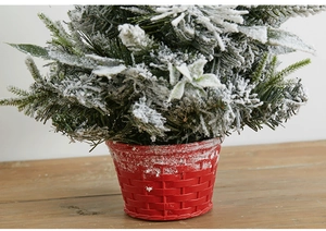 Close-up of a snow-flocked mini Christmas tree in a red woven texture pot on wood table