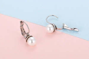 Detailed macro view of 18K gold plated pearl earrings with French hook design on a pastel base