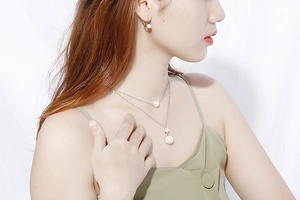 Detailed view of model wearing a layered silver necklace and matching pearl earrings
