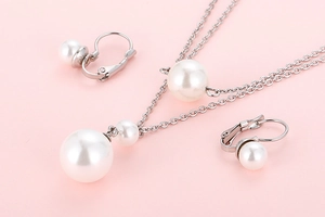 Macro detail of 18K gold plated pearl necklace and matching earrings on pink backdrop