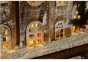 Close-up of wooden Christmas house with LED warm light and snowy texture details