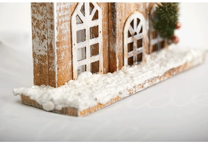 Close-up of wooden Christmas house with white snow base and green holiday accents