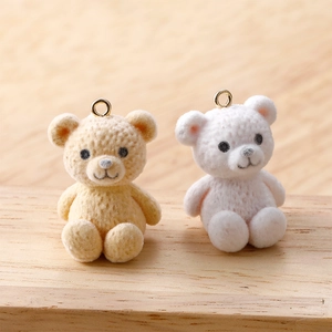 Close-up of beige and white plush teddy bear pendants with gold rings on wood surface