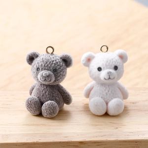 Close-up of grey and white flocked teddy bear charms with golden loops for jewelry making