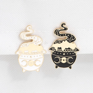 Macro detail of black and white enamel witch cauldron pins with moon phase patterns