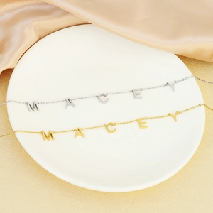 Detailed view of polished gold and silver MACEY letter necklaces on satin fabric