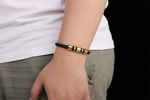 Detail of a braided black leather bracelet with gold and silver metal cylinders on wrist