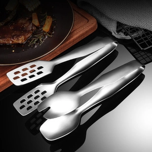 Close-up of four stainless steel kitchen food tongs on a professional kitchen counter