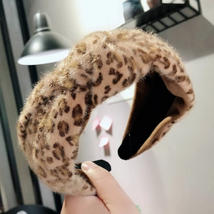Hand holding a plush leopard print headband with a wide knot design and soft brown fur