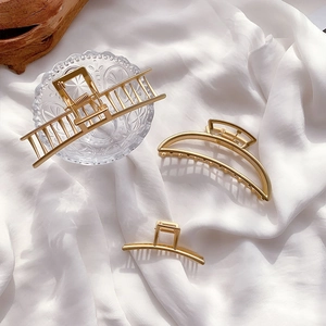 Three elegant gold metal hair claws in various geometric shapes on white fabric