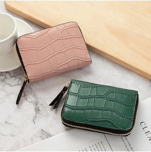 Pink and dark green crocodile-textured mini zip wallets on a stylish marble surface