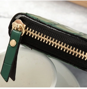Detail of dark green crocodile pattern leather wallet with premium gold zipper and rivet
