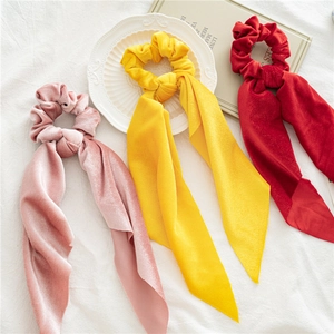 Three velvet bow scrunchies in pink, yellow, and red colors on white aesthetic background