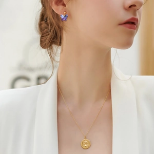 Detail of purple butterfly earrings and gold portrait medallion necklace on model