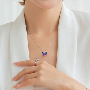 Close-up of a purple butterfly crystal pendant on silver chain and matching ring on model