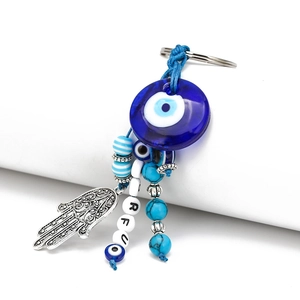 Detail of blue glass evil eye keychain with hamsa hand and turquoise beads on white background