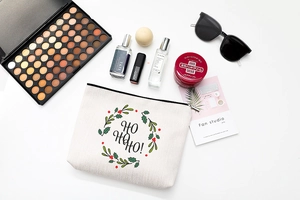 Flat lay of Ho Ho Ho Christmas canvas makeup bag with festive wreath and cosmetic items