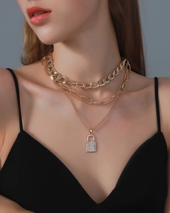 Detail of a triple-layered gold chain necklace with a zircon-encrusted padlock pendant