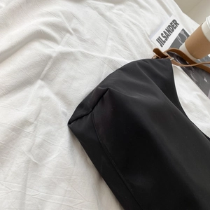 Minimalist black nylon tote bag with brown leather straps on a white fabric background