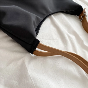 Close-up of black canvas tote bag with brown leather strap and metal buckle hardware