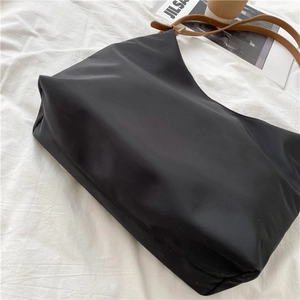 Detail of black nylon tote bag with brown leather shoulder straps on minimalist background